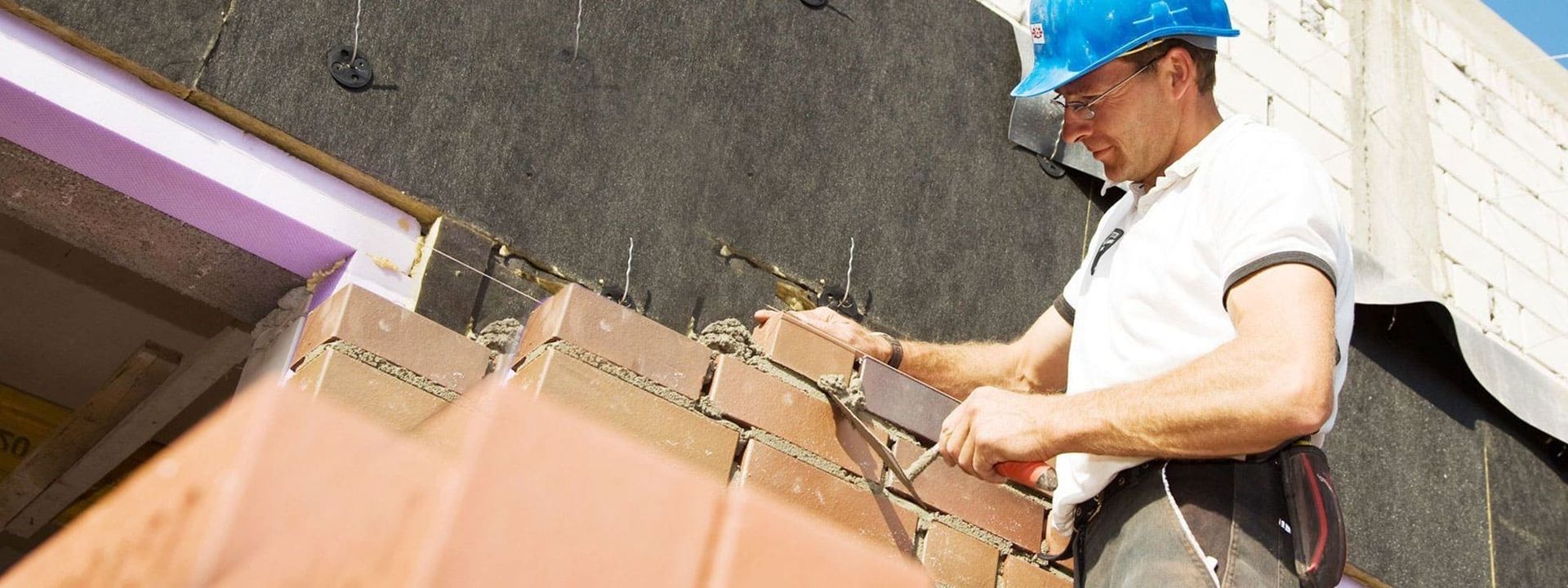 Ein Mann arbeitet konzentriert an einer Ziegelmauer und verlegt sorgfältig die Steine.